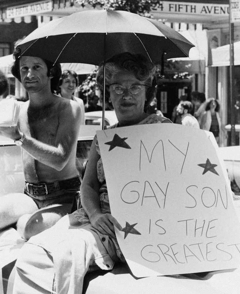 AI caption: a woman holding a sign that says my gay son is the greatest, black and white