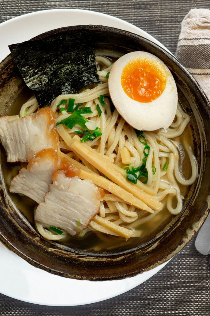 AI caption: a bowl of ramen with meat and egg on a table, asian