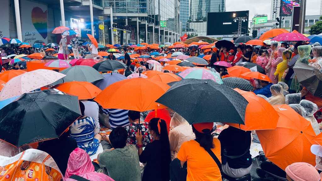 AI caption: a crowd of people sitting on the ground in front of a building, portrait a crowd of people with orange umbrellas on a street